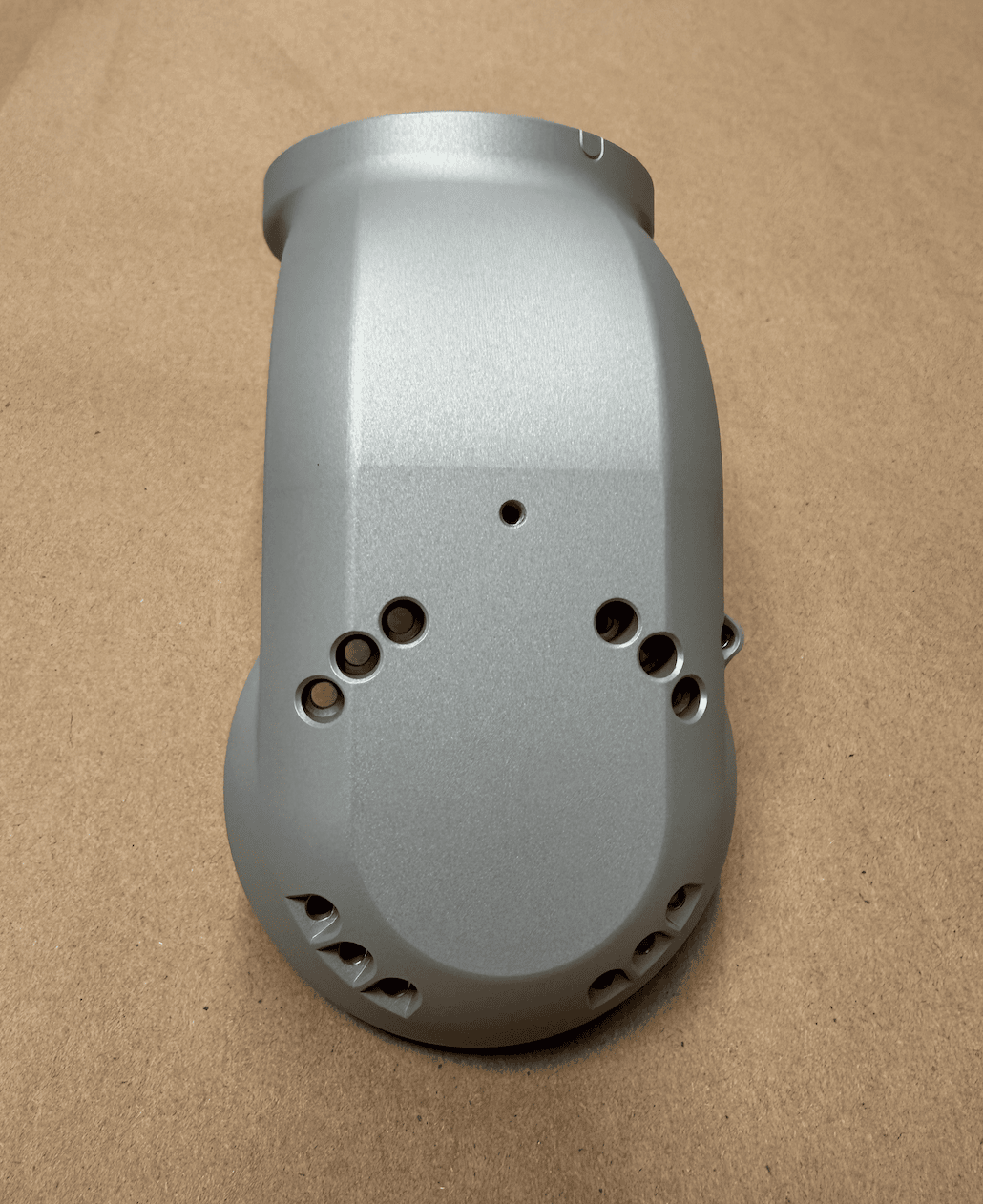 Machined metal joint component with precision-drilled holes and a matte silver finish on a kraft paper background